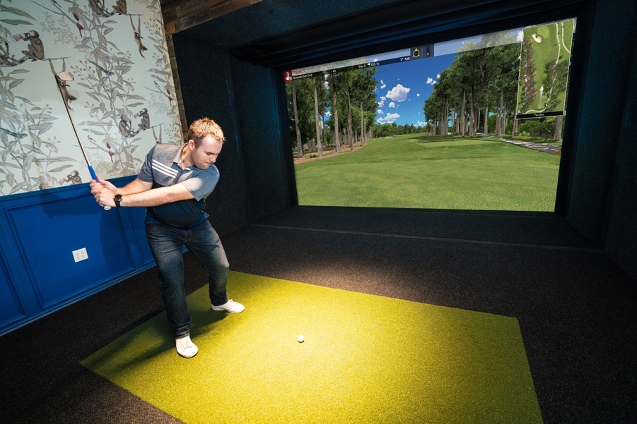 A man swinging a club in an at-home golf simulator.