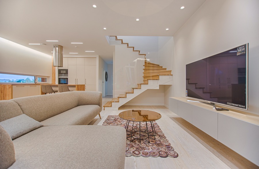 A beautiful, clean, modern living room featuring a large flatscreen television, recessed lighting and a winding staircase. 